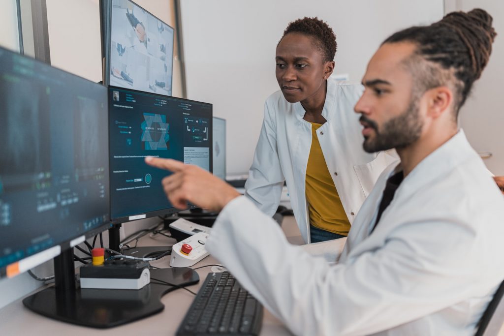 Two scientists in lab coats analyze data on computer screens in a modern laboratory setting, prioritizing health and safety. One points at the monitor while the other observes intently.