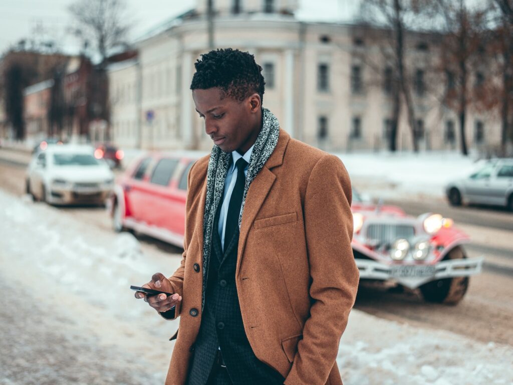 man wearing brown two-button dress jacket holding Android phone