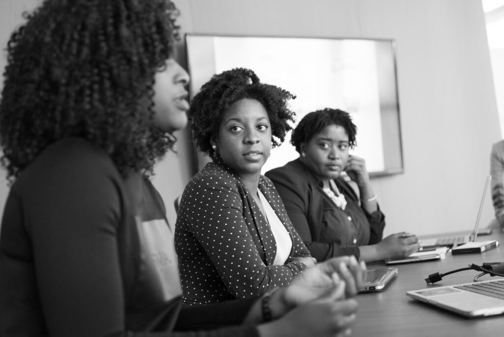 grayscale photography of two women on conference table looking at talking woman