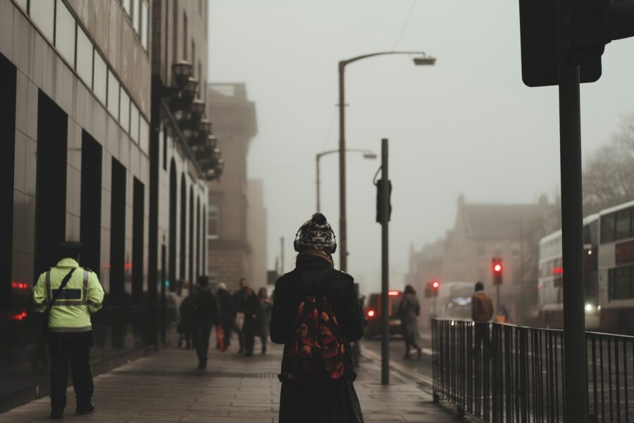 person wear black coat and backpack walking on sidewalk