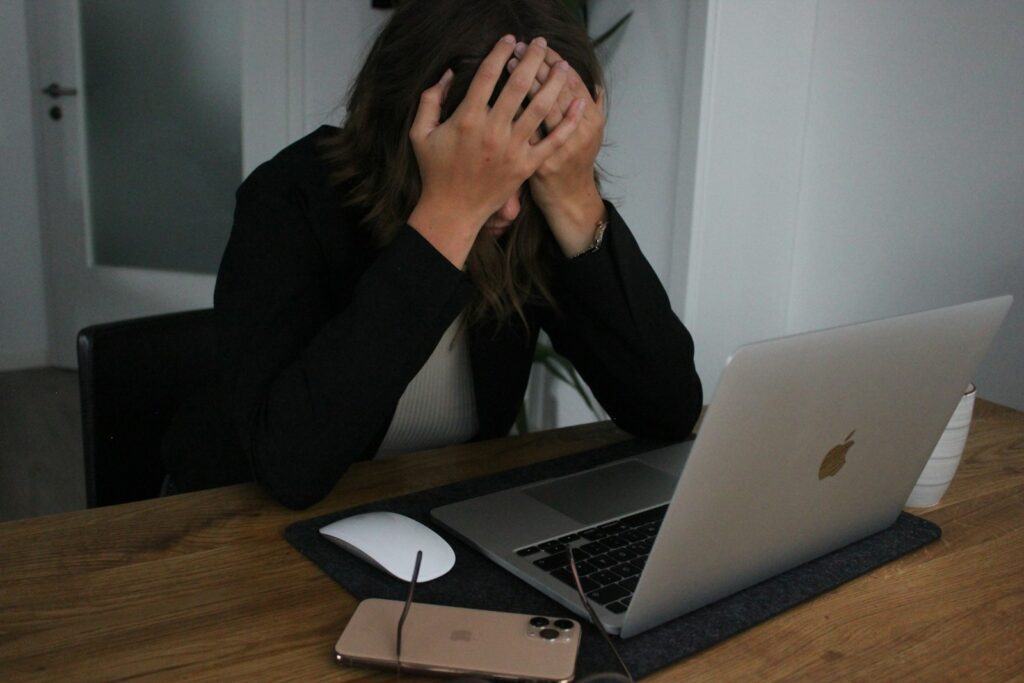 a woman covering her face while looking at a laptop