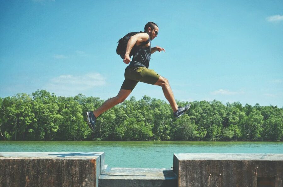 man leaping on concrete surface near body of water and forest at the distance during day