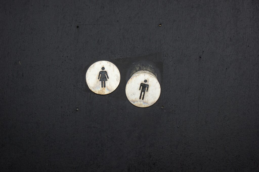 Two circular signs on a dark background depict restroom symbols: one for females (left) and one for males (right), promoting safety and wellbeing.