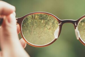 A hand holds a pair of glasses, enhancing visual accessibility by focusing on a clear view of trees through the lenses, with a blurred green background.