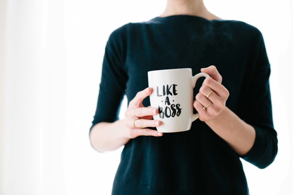 A person, seemingly unruffled by any panic around them, calmly holds a mug inscribed with "Like a Boss," their dark long-sleeve shirt adding to the composed aura.