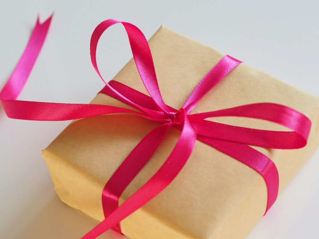 A brown gift box adorned with a vibrant pink ribbon bow sits elegantly on a white surface, embodying the charm of an incentive offering.