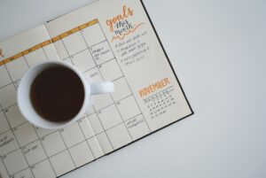 Open planner with handwritten goals for the month alongside a cup of coffee, set on a white surface. The planner highlights November, serving as a perfect time to assess data and reflect on progress.