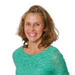 Beverlie Wilkinson, a woman with shoulder-length hair, smiles warmly at the camera in her turquoise lace top, set against a plain white background.