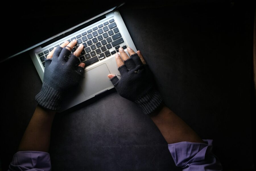 Hands wearing fingerless gloves type on a laptop keyboard against a dark background, perhaps crafting the perfect wish list for the holiday season.