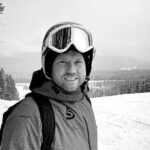 Gary Clark, in winter gear with a helmet and goggles, stands confidently on a snowy slope surrounded by trees.