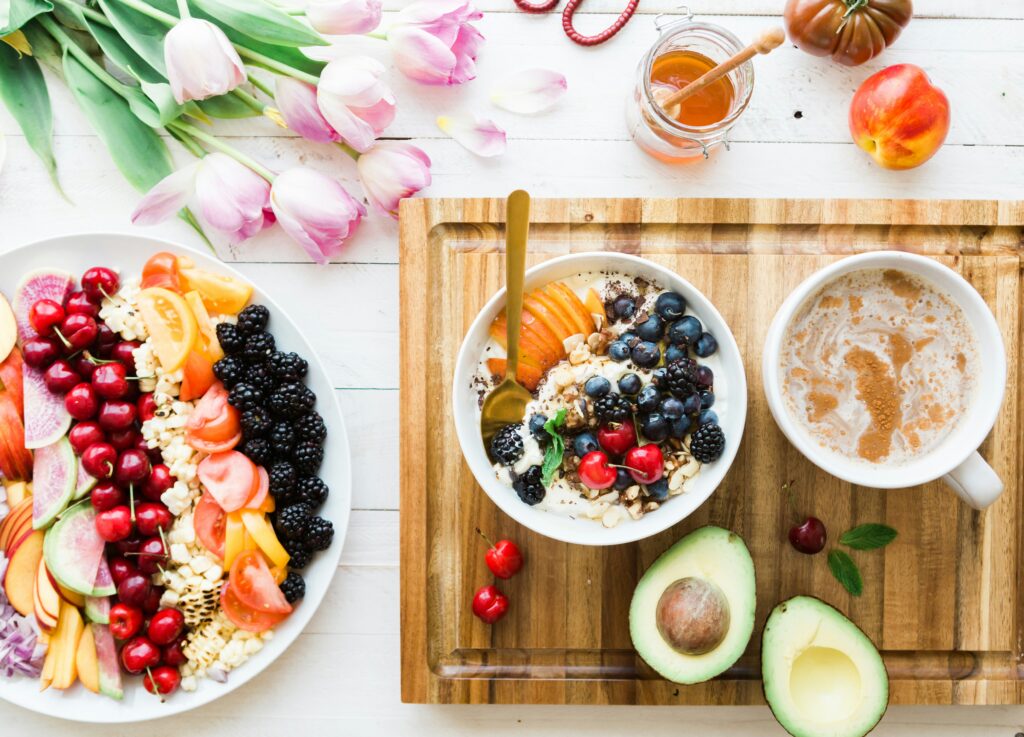 A tabletop adorned with vibrant fruit bowls, a cup of coffee, half an avocado for gut health, honey, and fresh tulips.