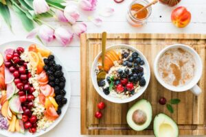 A tabletop adorned with vibrant fruit bowls, a cup of coffee, half an avocado for gut health, honey, and fresh tulips.