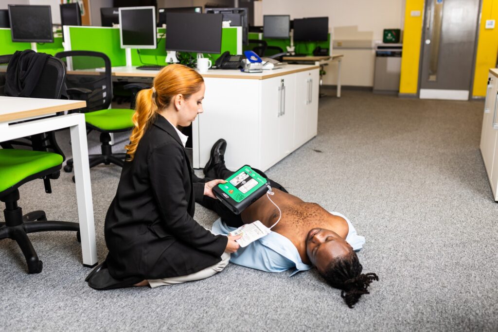 A person using a defibrillator on a person lying on an office floor.