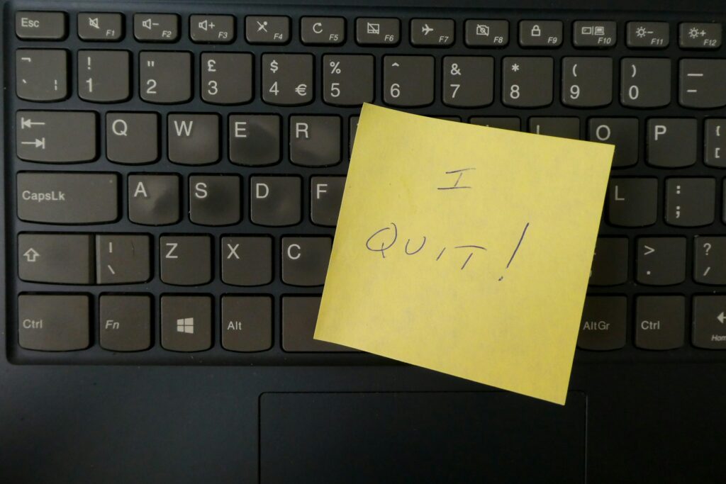 A yellow sticky note with the words "I QUIT!" is boldly placed on a laptop keyboard, signaling impending changes.