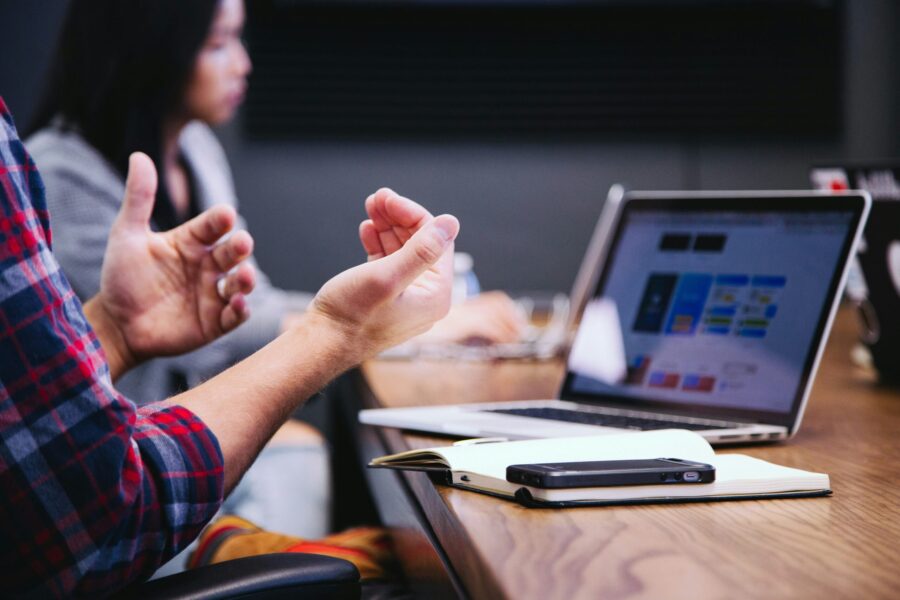 Two people sit at a table with a laptop and notebook. One gestures animatedly while discussing rewards and incentives, weaving ideas into the conversation.