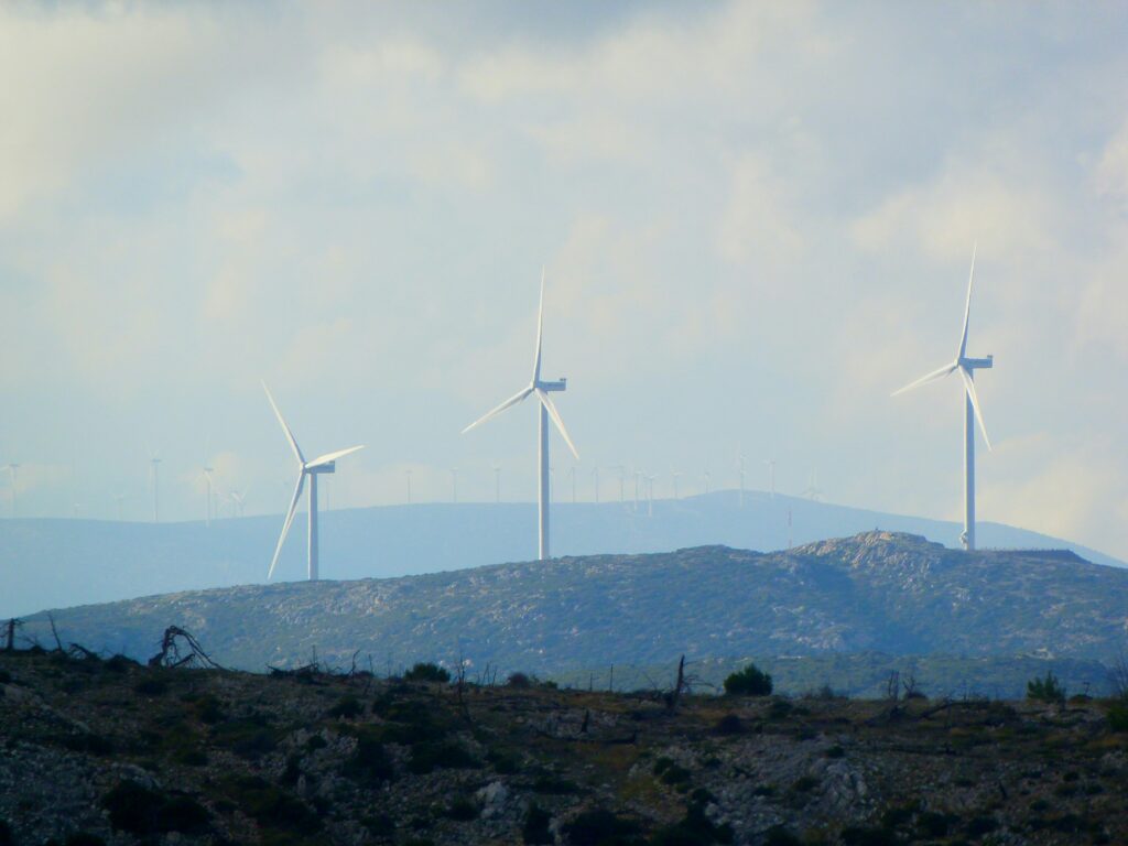 Against a backdrop of a partly cloudy sky, several wind turbines gracefully adorn the hilly landscape, showcasing a commitment to ESG principles and sustainable energy solutions.