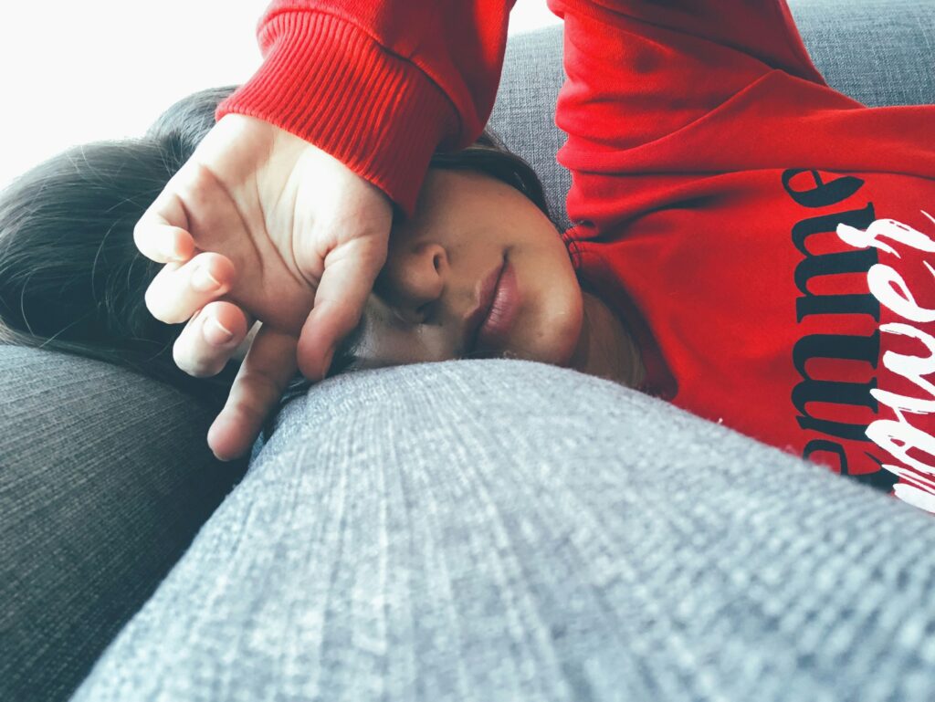 During the holiday season, a person in a cozy red sweater rests on a gray couch, one arm draped over their eyes.