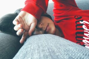 During the holiday season, a person in a cozy red sweater rests on a gray couch, one arm draped over their eyes.