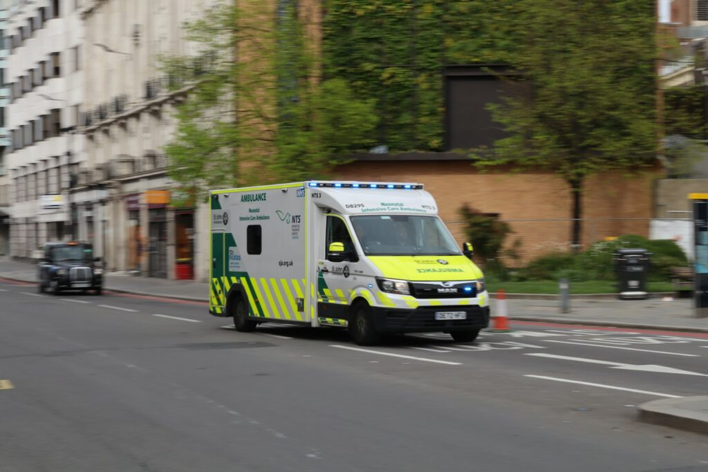 An ambulance driving down a city street next to tall buildings.