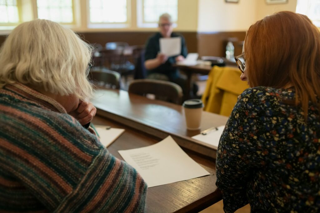 Two women sitting at a table with papers in front of them.