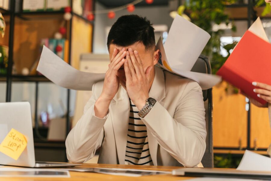 Stressed businessman overwhelmed by paperwork in office environment, demonstrating burnout.