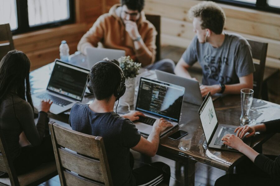 A group of office workers with laptops around a table.