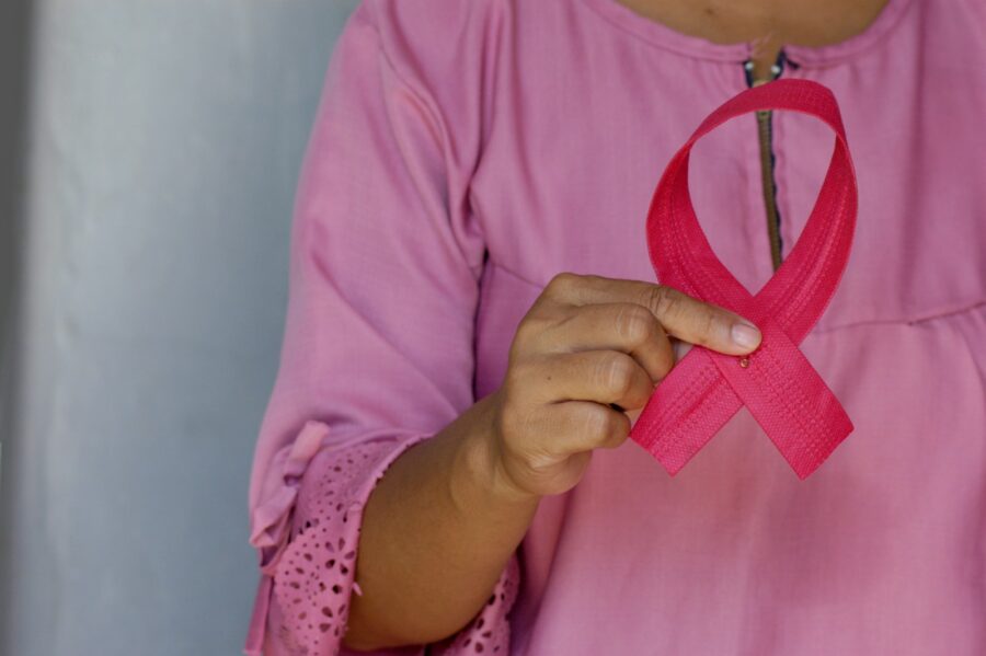 A woman in a pink shirt holding a cancer ribbon.