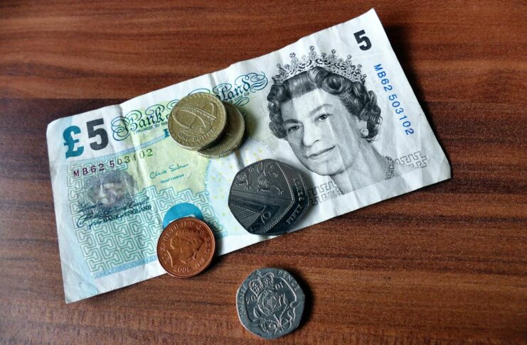 Close-up of a five-pound note and coins representing UK currency on a wooden surface.