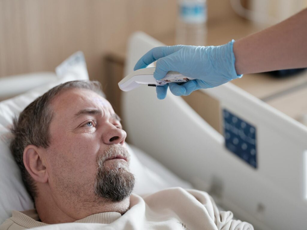 A healthcare professional measures the temperature of a patient using a non-contact thermometer in a hospital setting.