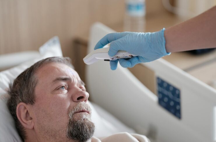 A healthcare professional measures the temperature of a patient using a non-contact thermometer in a hospital setting.