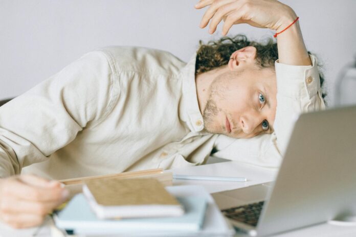 A tired Caucasian man at a desk, showing signs of exhaustion and stress, exemplifying workplace burnout.