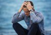 National Grief Awareness Week: Workplace Gaps in Bereavement Support A man in a plaid shirt sits by the water looking distressed, symbolizing stress.