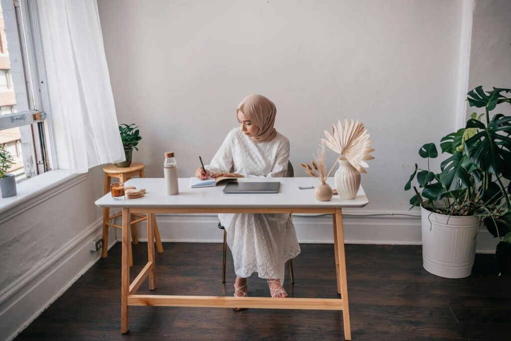 Woman in hijab taking notes in a calm, minimalist workspace with natural elements.