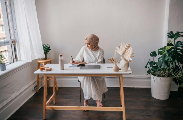 Woman in hijab taking notes in a calm, minimalist workspace with natural elements.