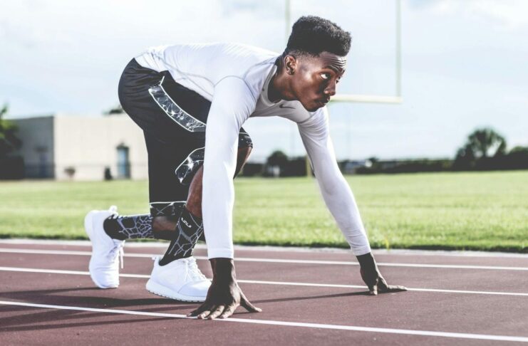 Focused athlete in starting position on a sunny track field, ready to sprint.