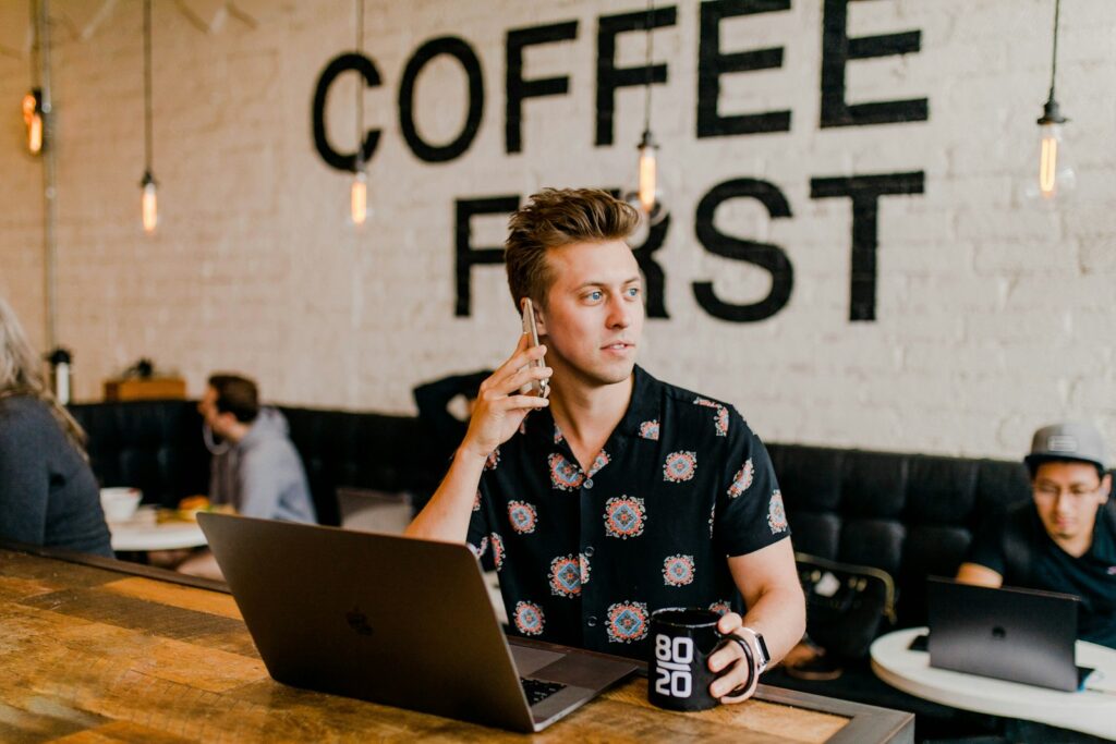 A man on the phone and with his laptop, at a cafe.