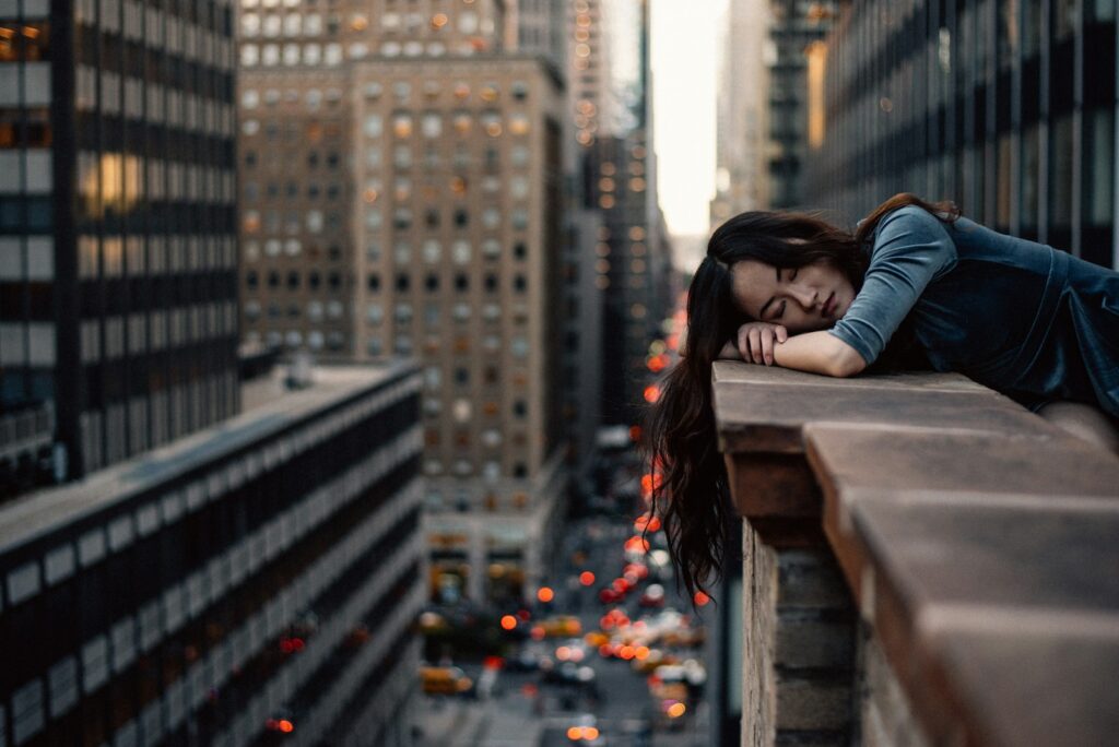 A young woman with her head on a highrise rail, indicating burnout