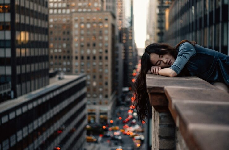 A young woman with her head on a highrise rail, indicating burnout