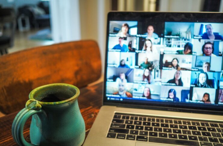 A laptop displaying a video meeting and mug of coffee on a table as a work from home setup.