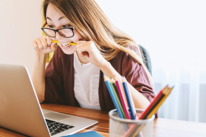 A stressed woman in front of a laptop and biting a pencil.