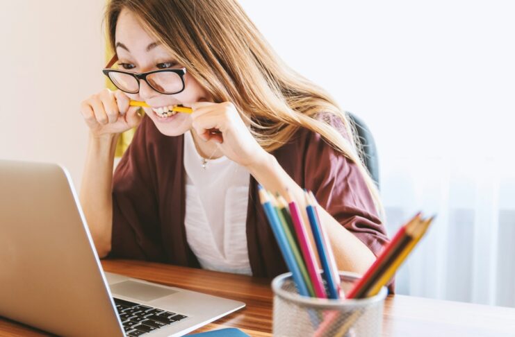 A stressed woman in front of a laptop and biting a pencil.