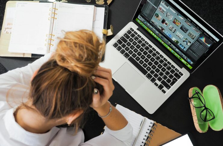Overhead view of a stressed woman working at a desk with a laptop, phone, and notebooks.