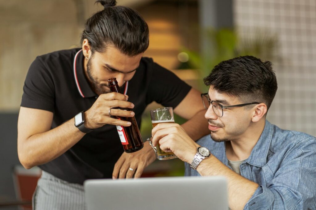 Two men drinking while working at a laptop.