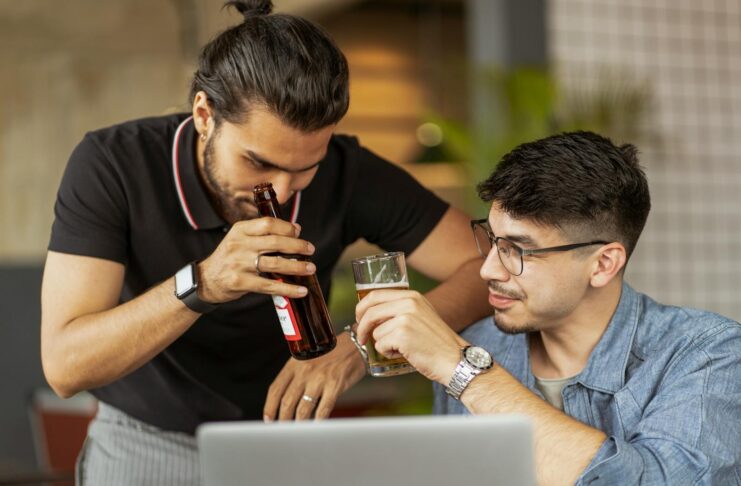 Two men drinking while working at a laptop.