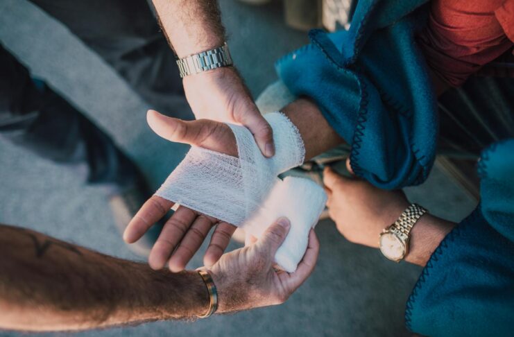 Close-up of two people bandaging an injured hand outdoors, focusing on first aid care.