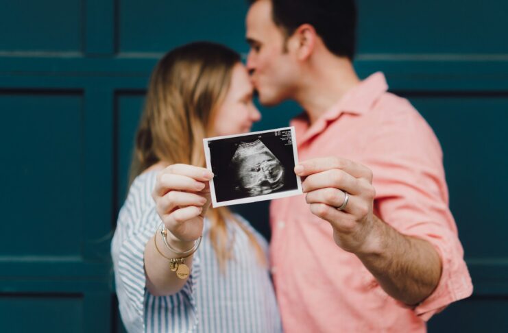 man kissing woman's forehead white holding ultrasound photo