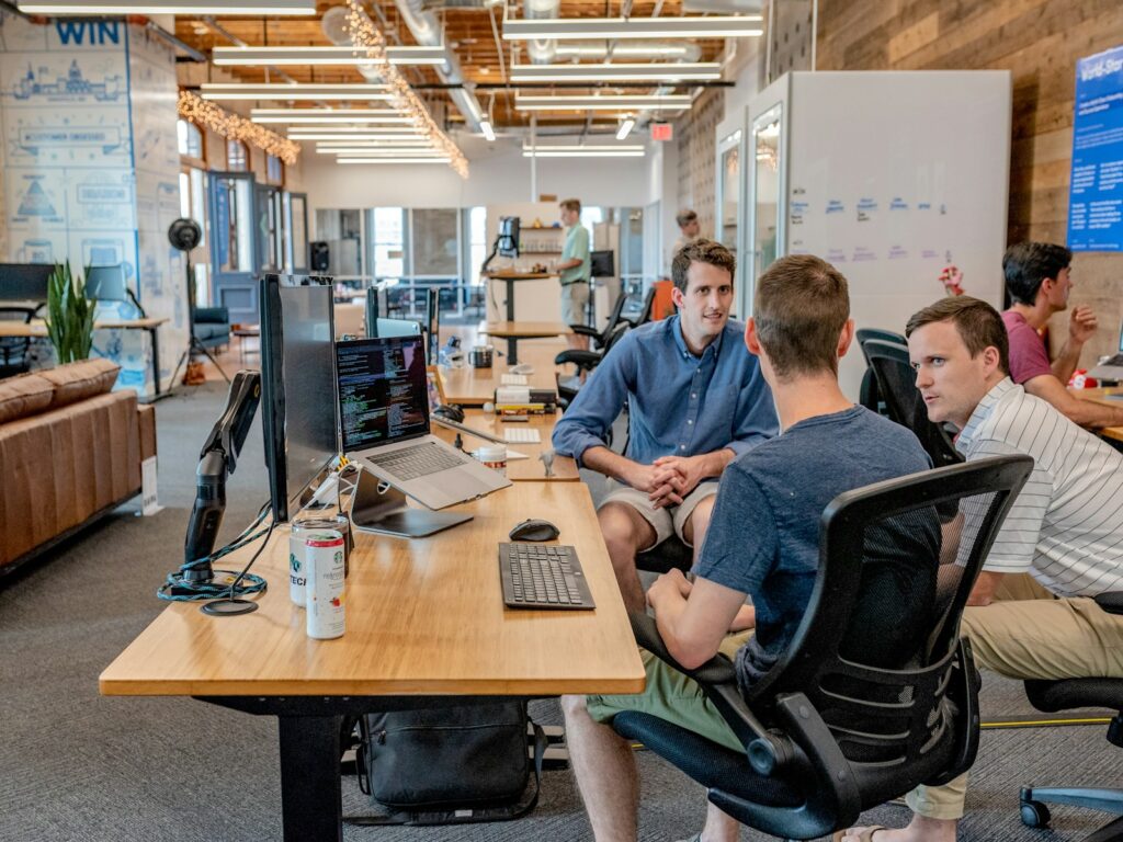 Three men sitting by an office desk with computers.