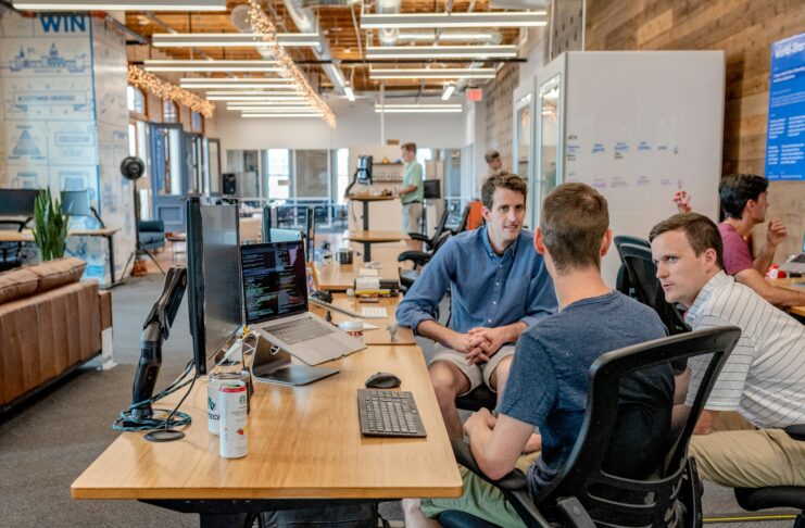 Three men sitting by an office desk with computers.