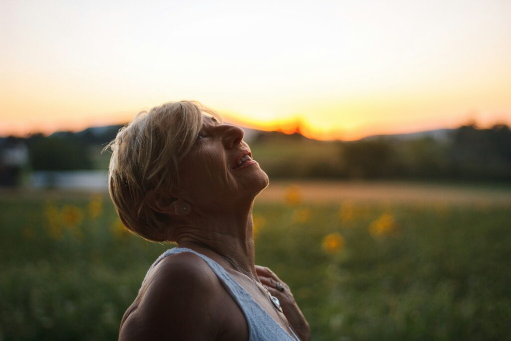 A middle-aged woman in white tank top looking at the sunset.