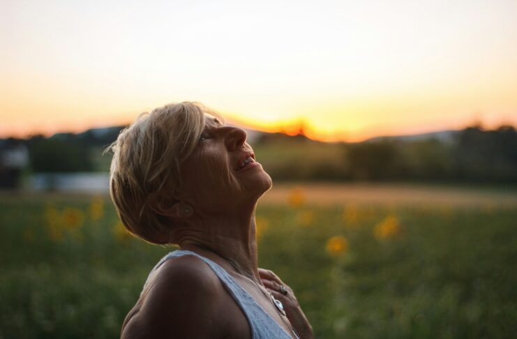 A middle-aged woman in white tank top looking at the sunset.